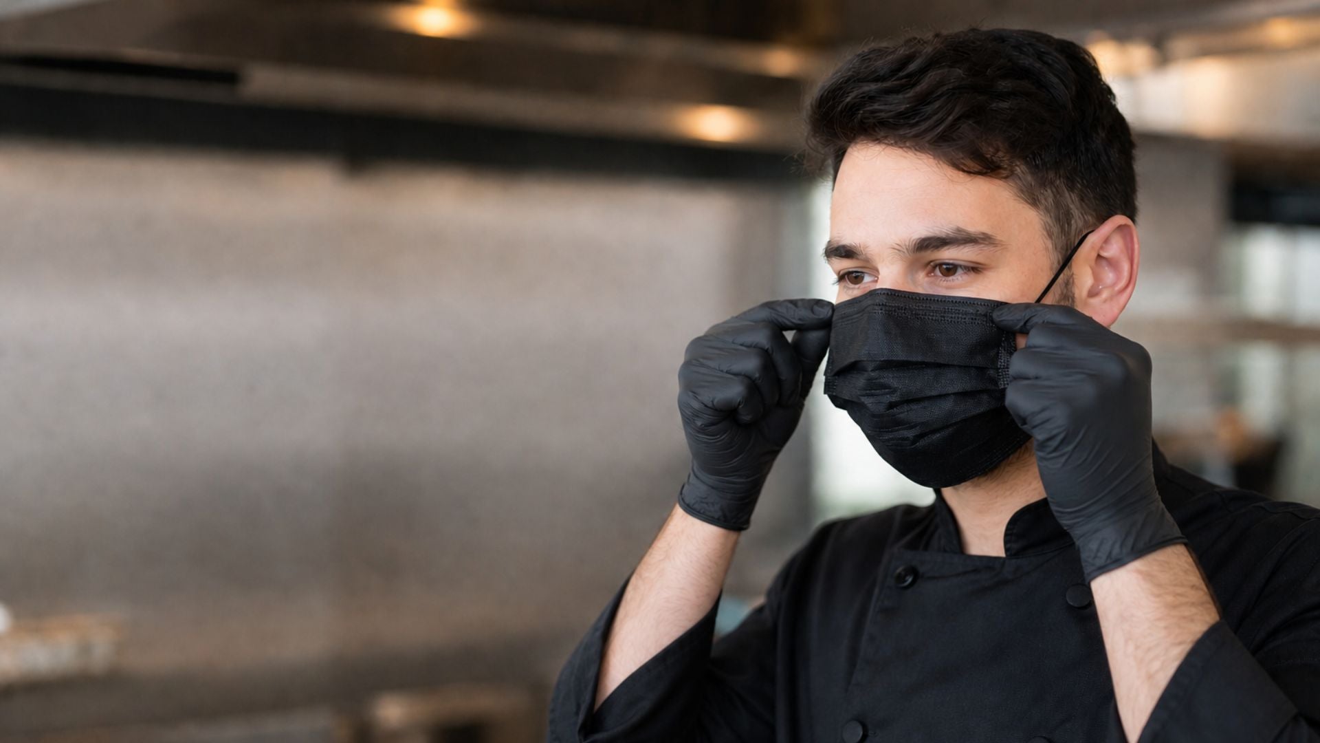 Profesional en cocina ajustando cubrebocas negro desechable con guantes de nitrilo negros
