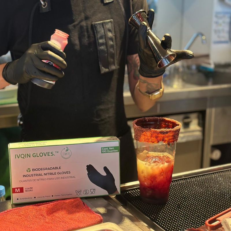 Bartender utilizando guantes de nitrilo negros mientras prepara una bebida, mostrando uso profesional en contacto con alimentos